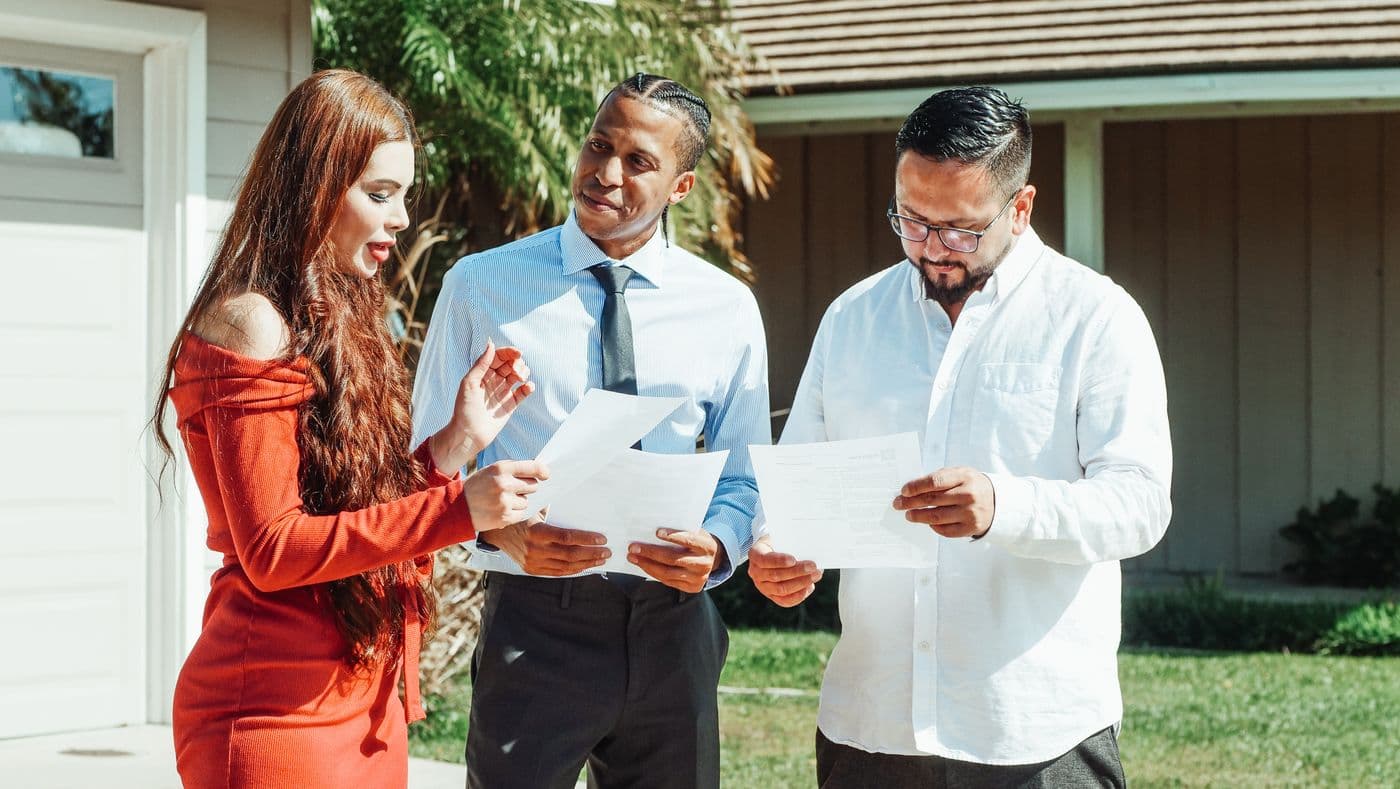 Buyers and an agent reviewing closing papers in front of a house